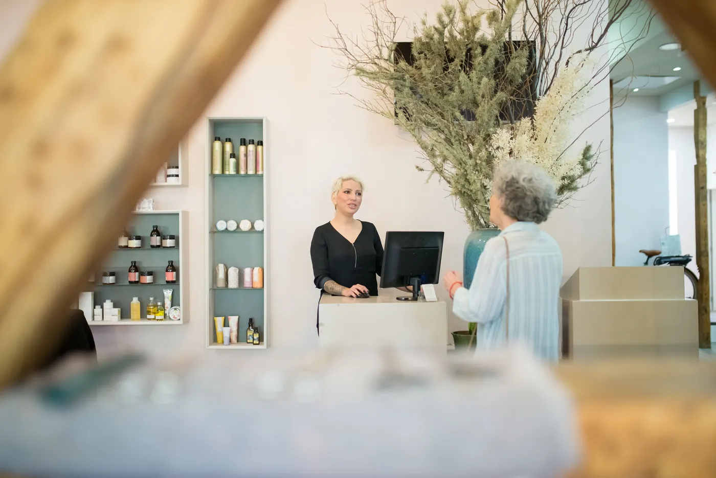 A salon receptionist speaks with a client at the reception counter.