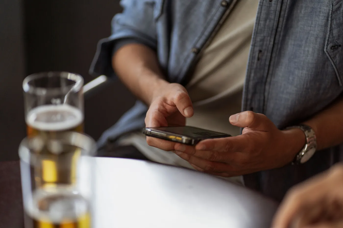 A person holding a smartphone at a café table beside drinks.